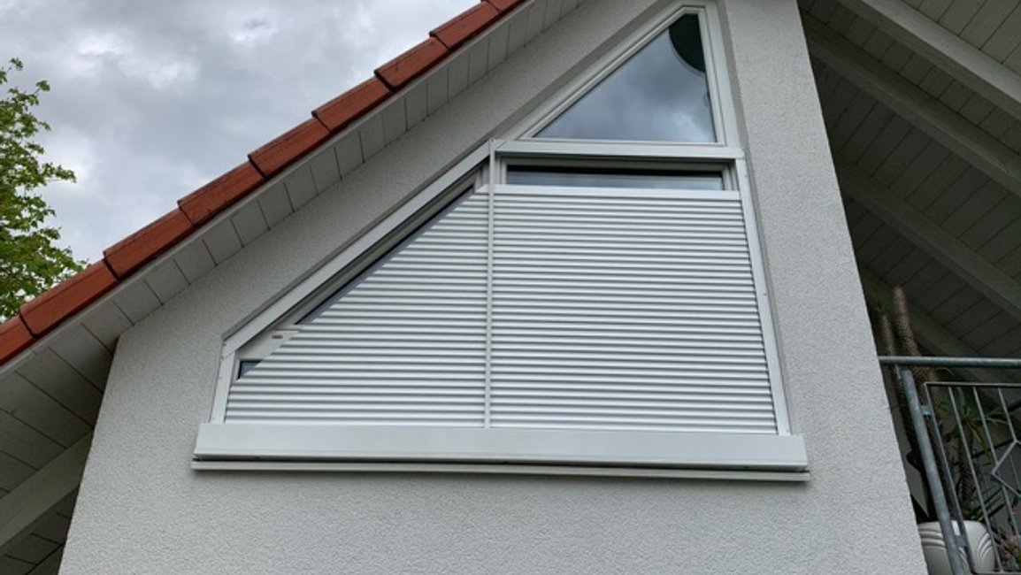 „Šikmé venkovní žaluzie na moderním rodinném domě – lomená fasáda se štítovým prosklením a zimní zahrada jsou zastíněné antracitovými žaluziemi, které kopírují sklon střechy