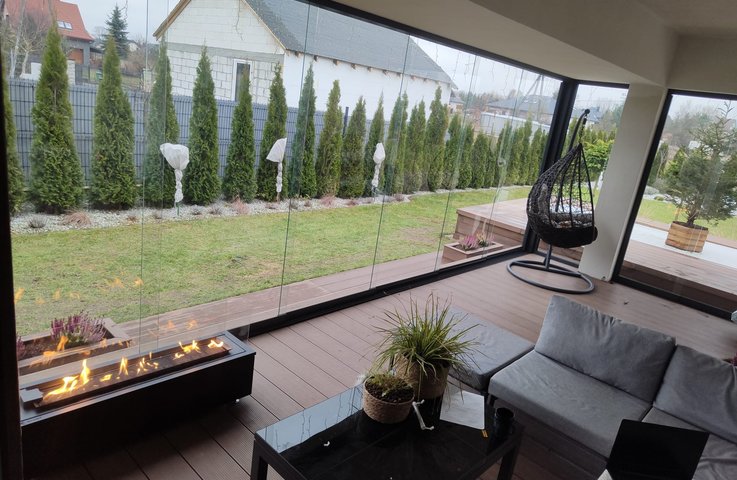 Zasklená terasa s bezrámovým zasklením a biokrbem vytváří útulný celoroční obývák na zahradě