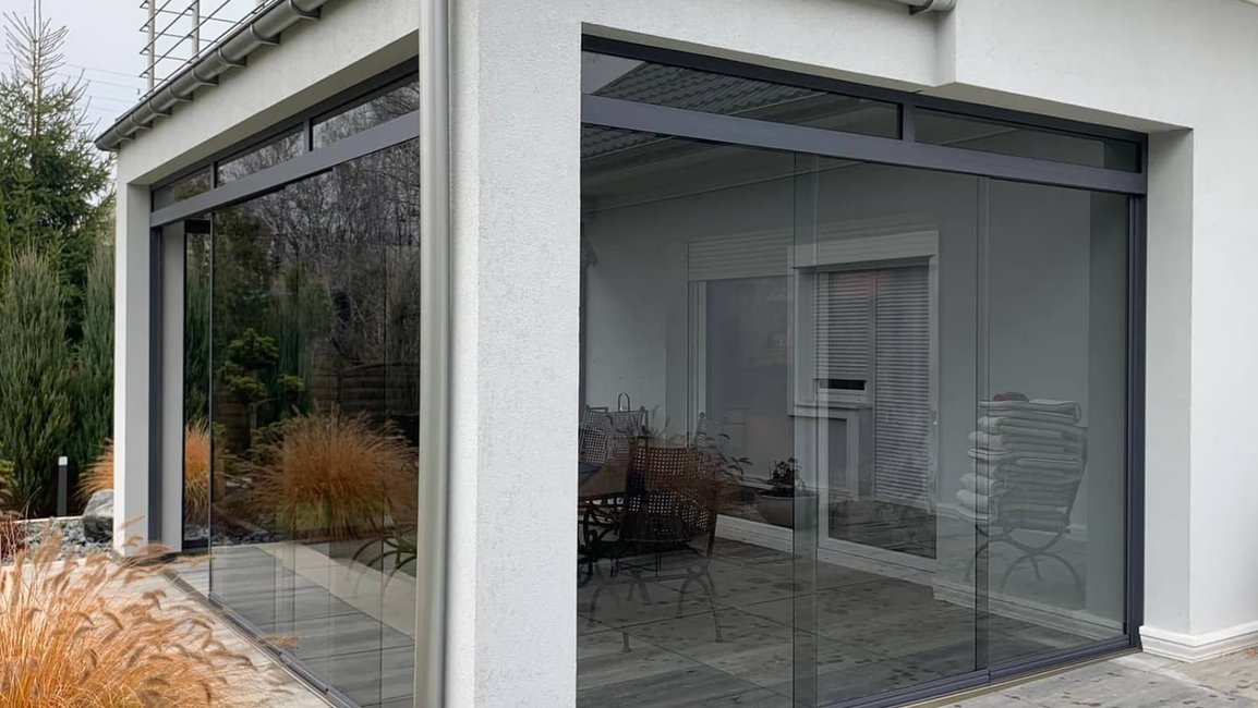 Elegantní bezrámové zasklení zimní zahrady v moderním designu. Prosklené stěny s maximální průhledností zajišťují dokonalé propojení interiéru s exteriérem. Ideální řešení pro zimní zahrady, pergoly a terasy od Hezký stín – kombinace estetiky, funkčnosti a nadčasového vzhledu.