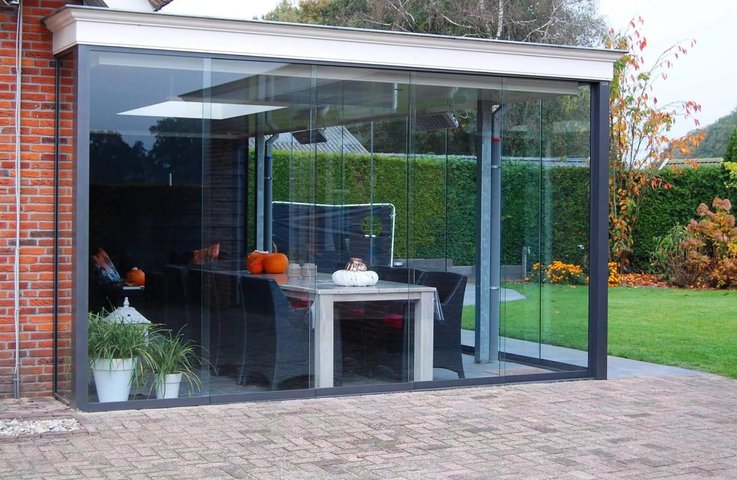 Bezrámové zasklení terasy u rodinného domu – moderní skleněná stěna chrání venkovní jídelní kout a umožňuje výhled do zahrady za každého počasí.