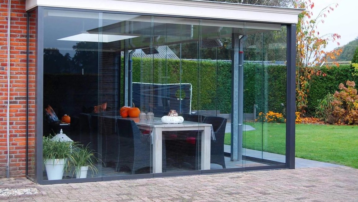 Bezrámové zasklení terasy u rodinného domu – moderní skleněná stěna chrání venkovní jídelní kout a umožňuje výhled do zahrady za každého počasí.