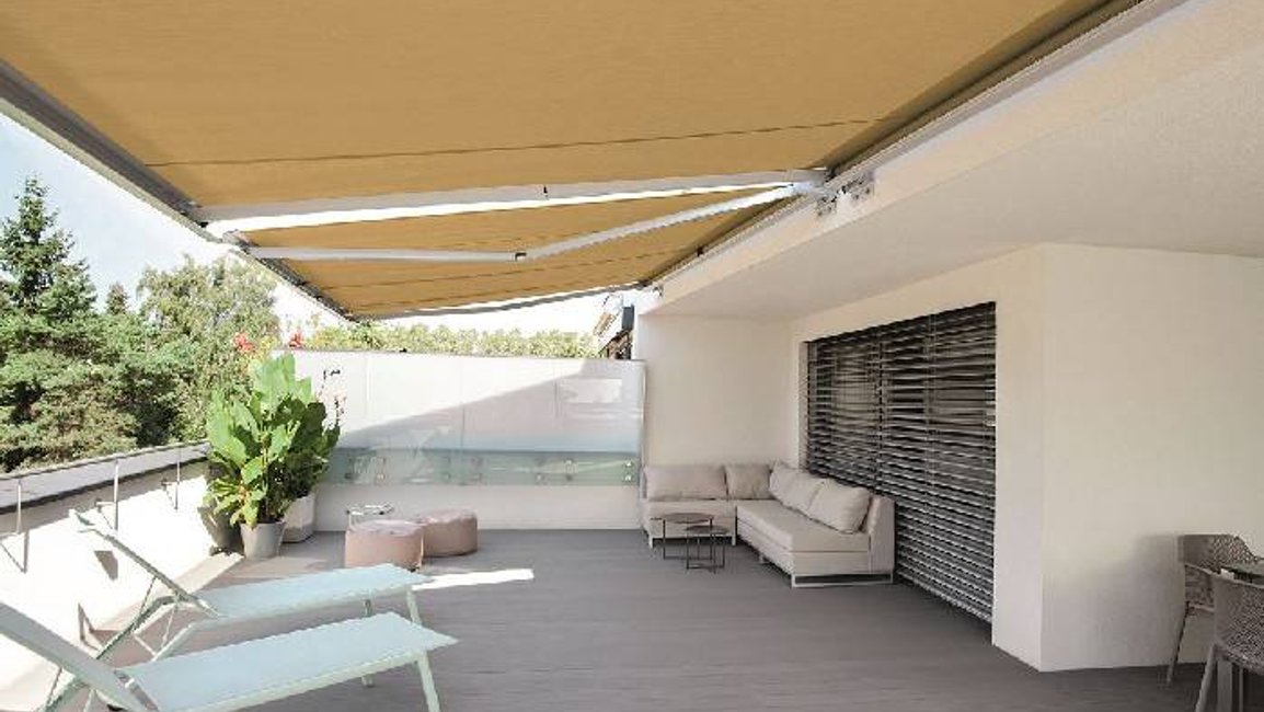 Výsuvná markýza od Hezký stín vytváří na prostorné střešní terase příjemný stín pro relax na lehátkách i pohodlné sezení v rohové sedačce.