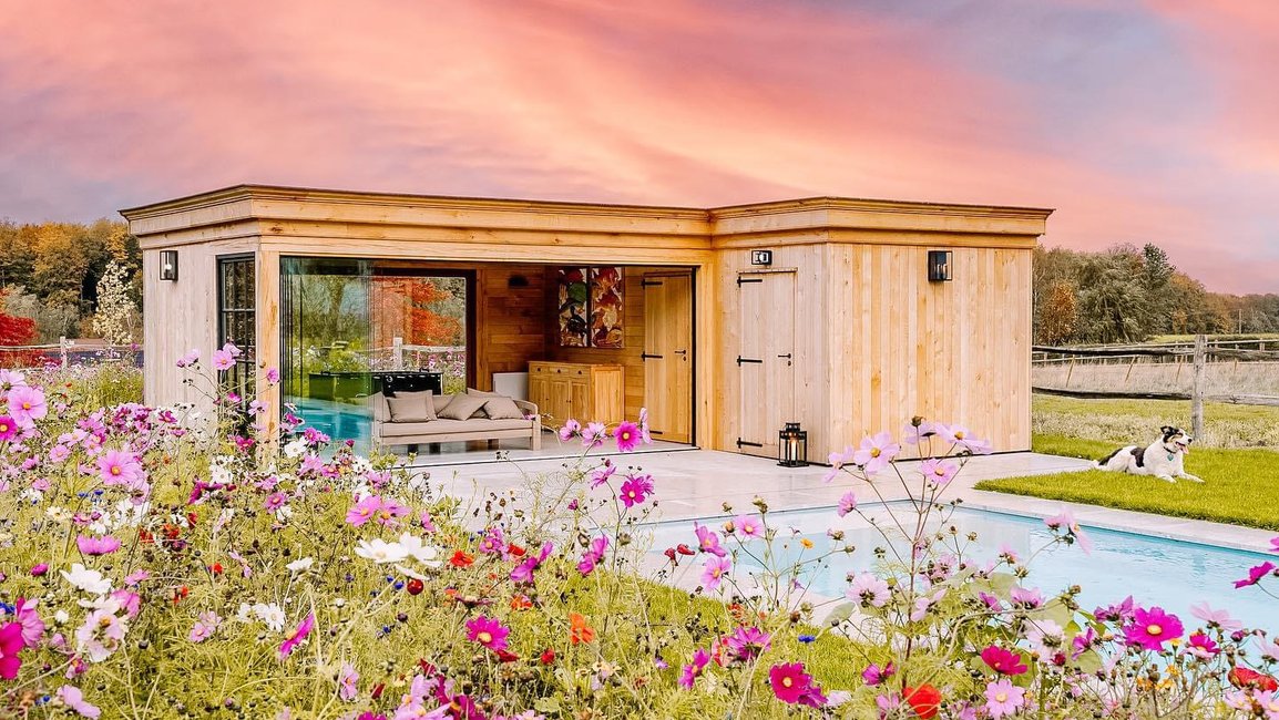 Bezrámově zasklený dřevěný zahradní pavilon u bazénu, který rozšiřuje terasu a chrání posezení před počasím.