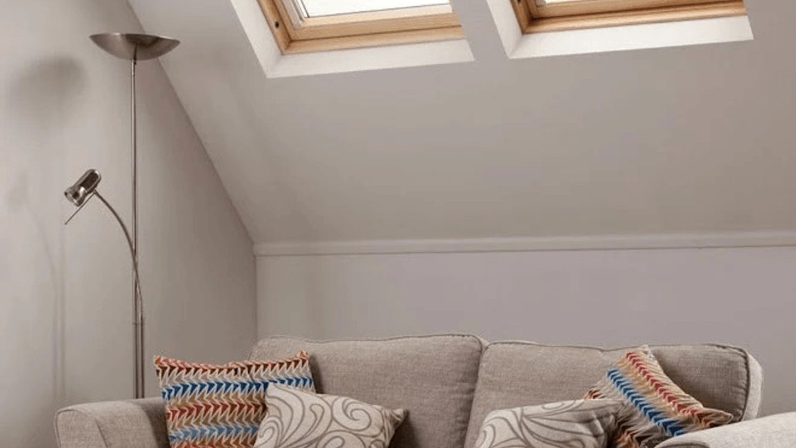 Podkrovní obývací pokoj s dvojicí střešních oken vybavených zatemňovacími roletami. Rolety zlepšují stínění, brání přehřívání místnosti a vytvářejí příjemné prostředí pro odpočinek i večerní hraní na kytaru.