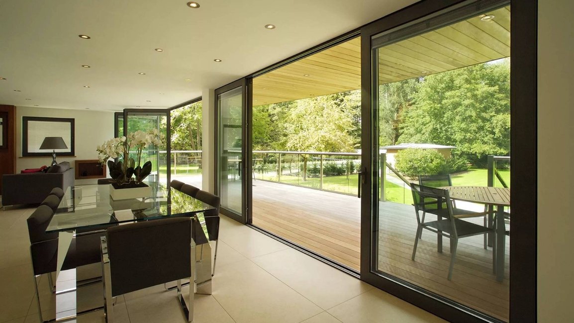 Moderní interiér s velkoformátovými hliníkovými posuvnými dveřmi, které plynule propojují obývací pokoj s terasou a zahradou a do domu přivádějí maximum denního světla.