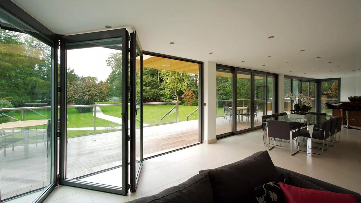 Skládací prosklený systém mezi obývacím pokojem a terasou – velkoformátové hliníkové dveře otevřené do zahrady, které spojují interiér s exteriérem a rozšiřují obytný prostor.