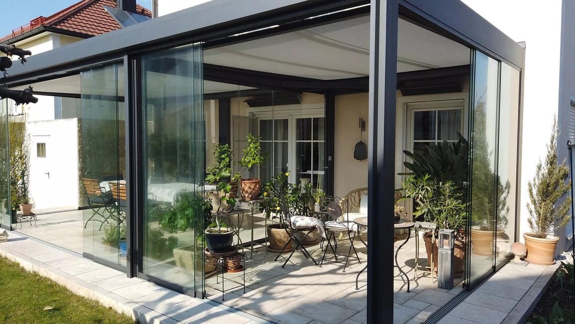 Plně zasklený hliníkový systém Hezký stín – prosklená pergola u rodinného domu proměněná v útulné posezení se zelení, chráněné před větrem a deštěm.