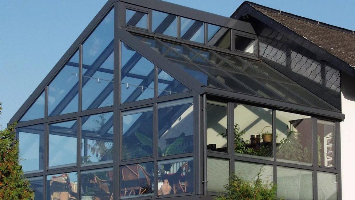 Velkorysá celoroční zimní zahrada z hliníku a skla v patře rodinného domu, s vysokým šikmým prosklením a výhledem do okolí – realizace Hezký stín.